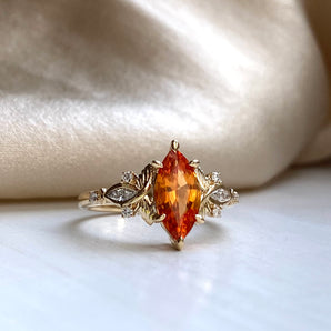 Gold engagement ring with vivid orange gem, narrow pointed marquise cut, surrounded by delicate gold and diamond butterflies on the sides. Nature inspired fantasy ring.
Medium to large size
