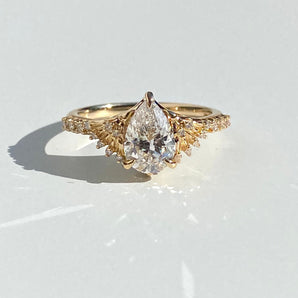 gold engagement ring with sparkling colorless pear diamond center supported by intricate spread wings design made of carved gold and diamonds. Overall size is medium