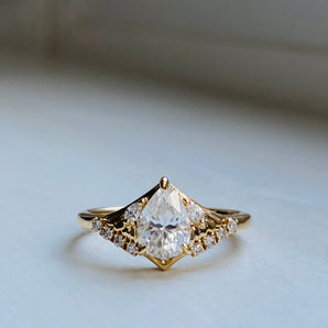 Gold ring with a large pear cut diamond center, supported by moth wings made of carved gold and encrusted with smaller diamonds on the edges