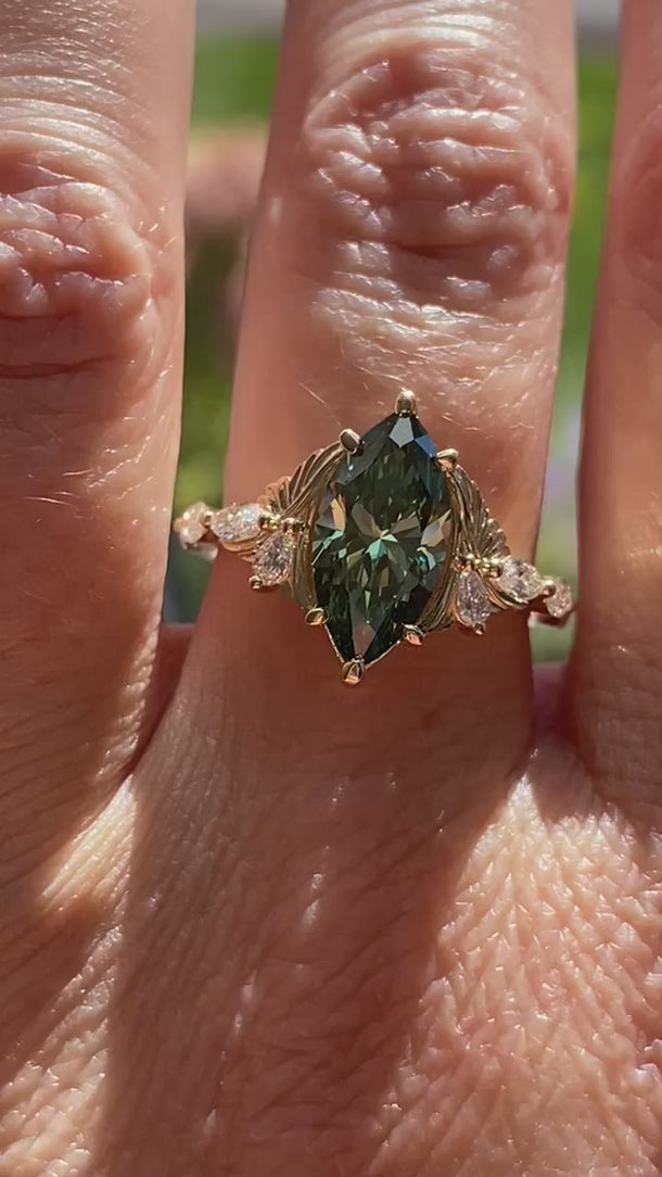 EidelPrecious Fiore Alpha + Beta 2ct green marquise lab diamond engagement ring worn on a hand, showcasing its elegant proportions, hummingbird-inspired 14k yellow gold setting and sparkling lab diamond accents.